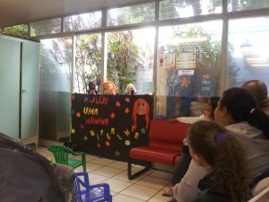 Adultos e crianças assistem ao teatro de fantoches na brinquedoteca. (Acervo Nupad)