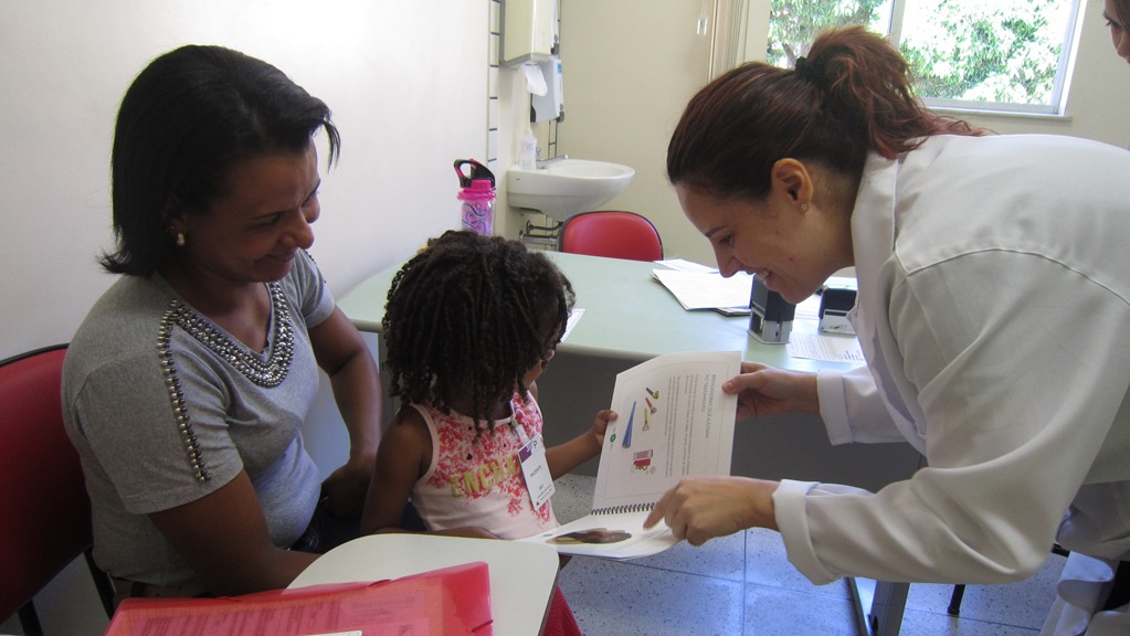 Maria Gabriela recebe cartilha de fibrose cística da nutricionista do Nupad, Michelle Alves, produzida pelo Ceaps em parceria com os Centros de Referência de MG. Foto: Rafaella Arruda.